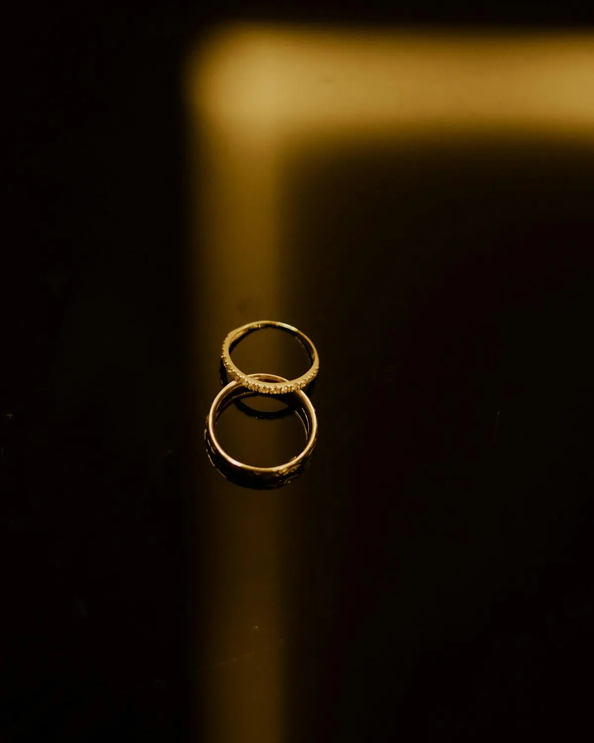 Two gold rings on a dark reflective surface